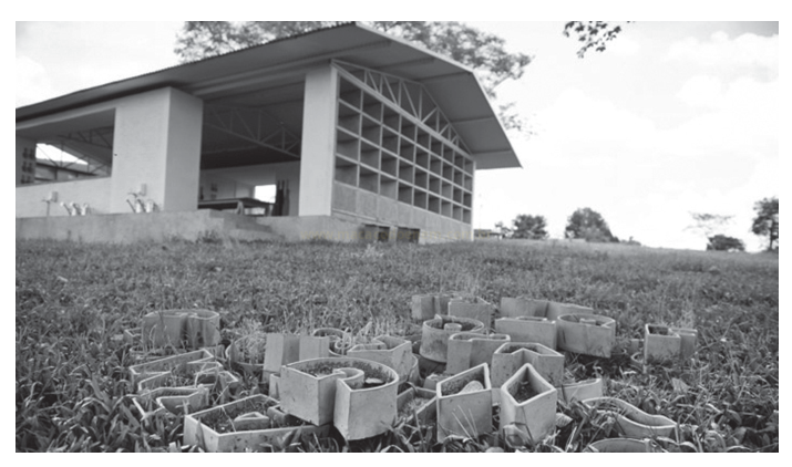 Fotografia em preto e branco de blocos de concreto vazados sobre a grama diante de um edifício de fachada envidraçada.