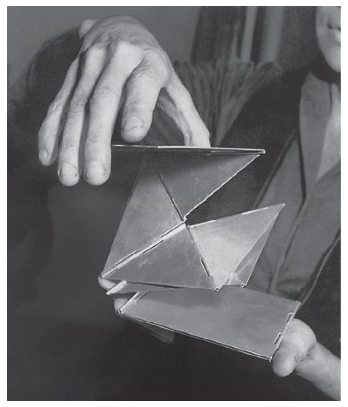Fotografia em preto e branco de duas mãos segurando um objeto geométrico dobrável de painéis triangulares e retangulares.
