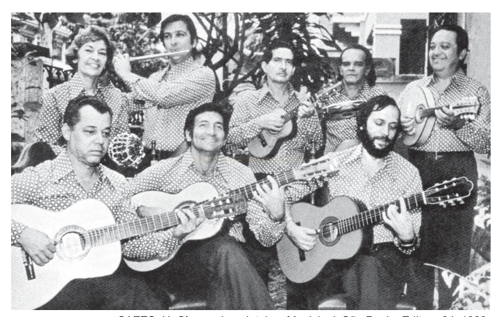 Fotografia em preto e branco de um grupo de oito músicos de camisas estampadas tocando violões, flauta e cavaquinho.