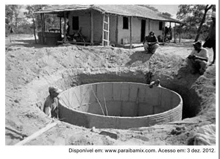 Fotografia em preto e branco de trabalhadores construindo uma cisterna circular de alvenaria em uma escavação, com uma casa simples ao fundo.