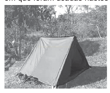 Fotografia em preto e branco de uma barraca de camping triangular montada em área de vegetação.