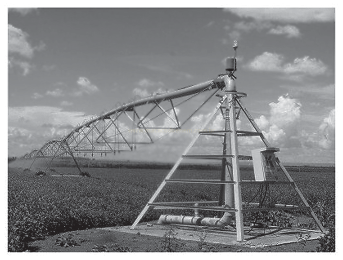 Fotografia em preto e branco de um pivô de irrigação sobre plantação, com torre de sustentação em destaque à direita.