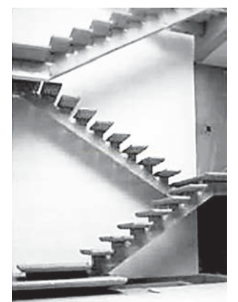 Fotografia em preto e branco de escadas em diagonal entre paredes claras, em composição geométrica.
