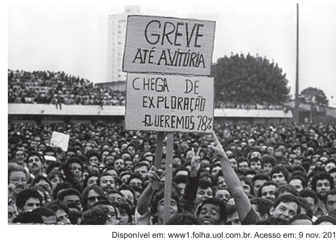 Fotografia em preto e branco de multidão segurando faixas de greve com pedido de aumento salarial.