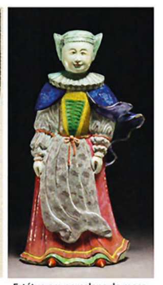 Fotografia de uma estatueta de cerâmica esmaltada de uma figura humana com capa azul e saia vermelha.