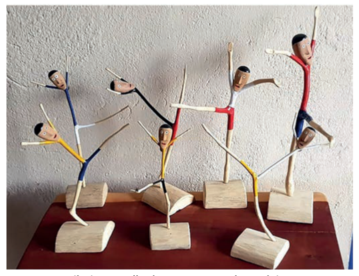 Fotografia de seis esculturas de madeira de figuras humanas estilizadas em poses de dança sobre uma mesa.