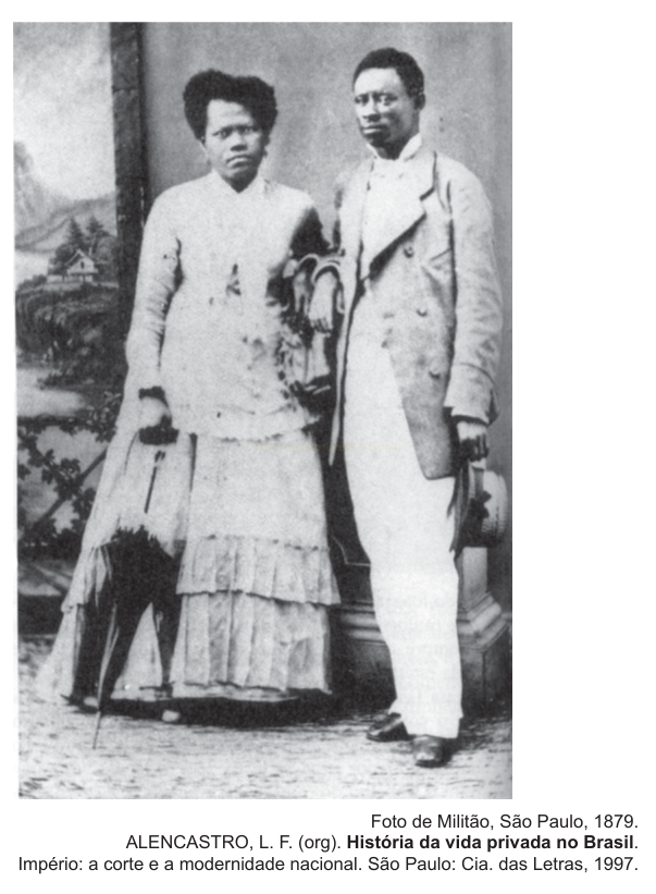 Fotografia antiga em preto e branco de um casal em estúdio, com cenário pintado ao fundo.