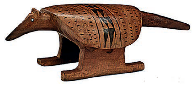 Escultura de madeira de um animal de focinho longo, decorada com padrões geométricos pintados em preto.