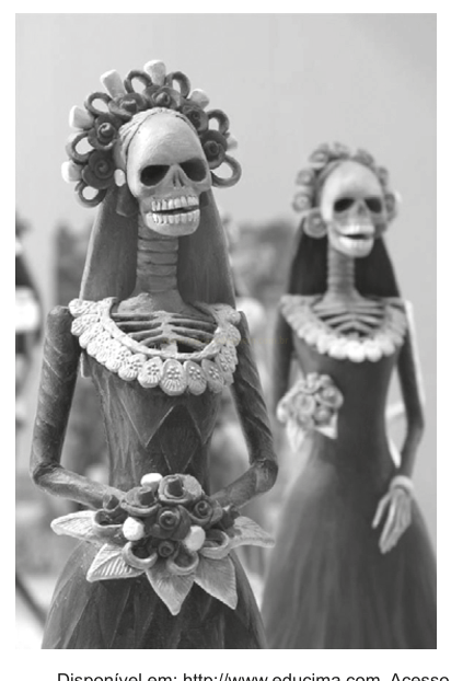 Fotografia em preto e branco de duas figuras esqueléticas vestidas com roupas elegantes, toucados de flores e buquês.
