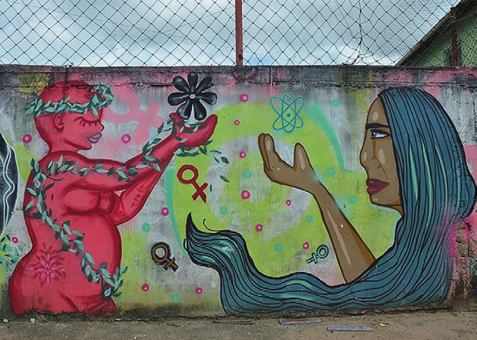 Grafite em muro com figura feminina rosa coberta de folhas e rosto feminino de cabelos azuis, cercados por símbolos femininos.